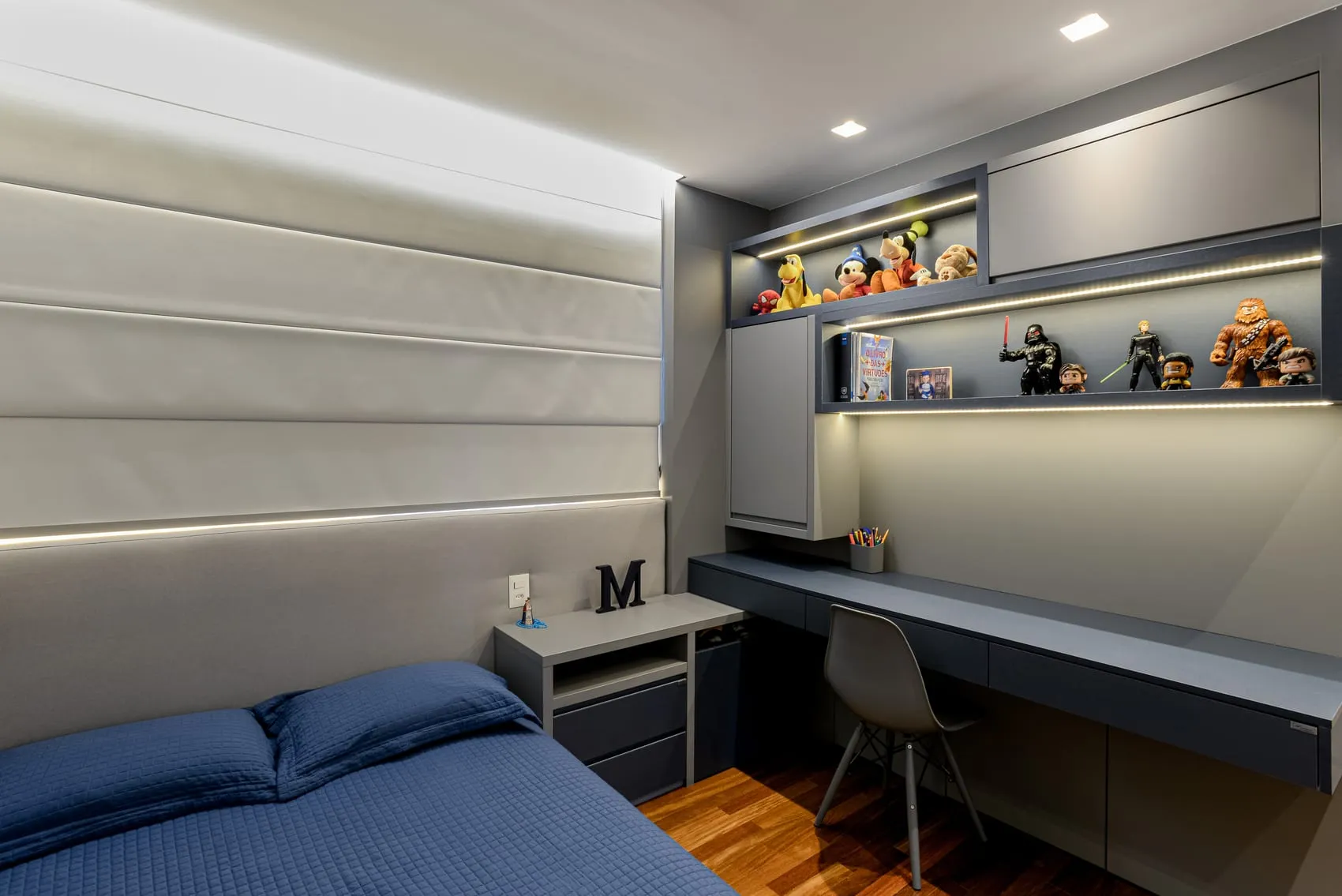 Quarto com cama azul, bancada de estudos escura, prateleira e coleção de bonecos