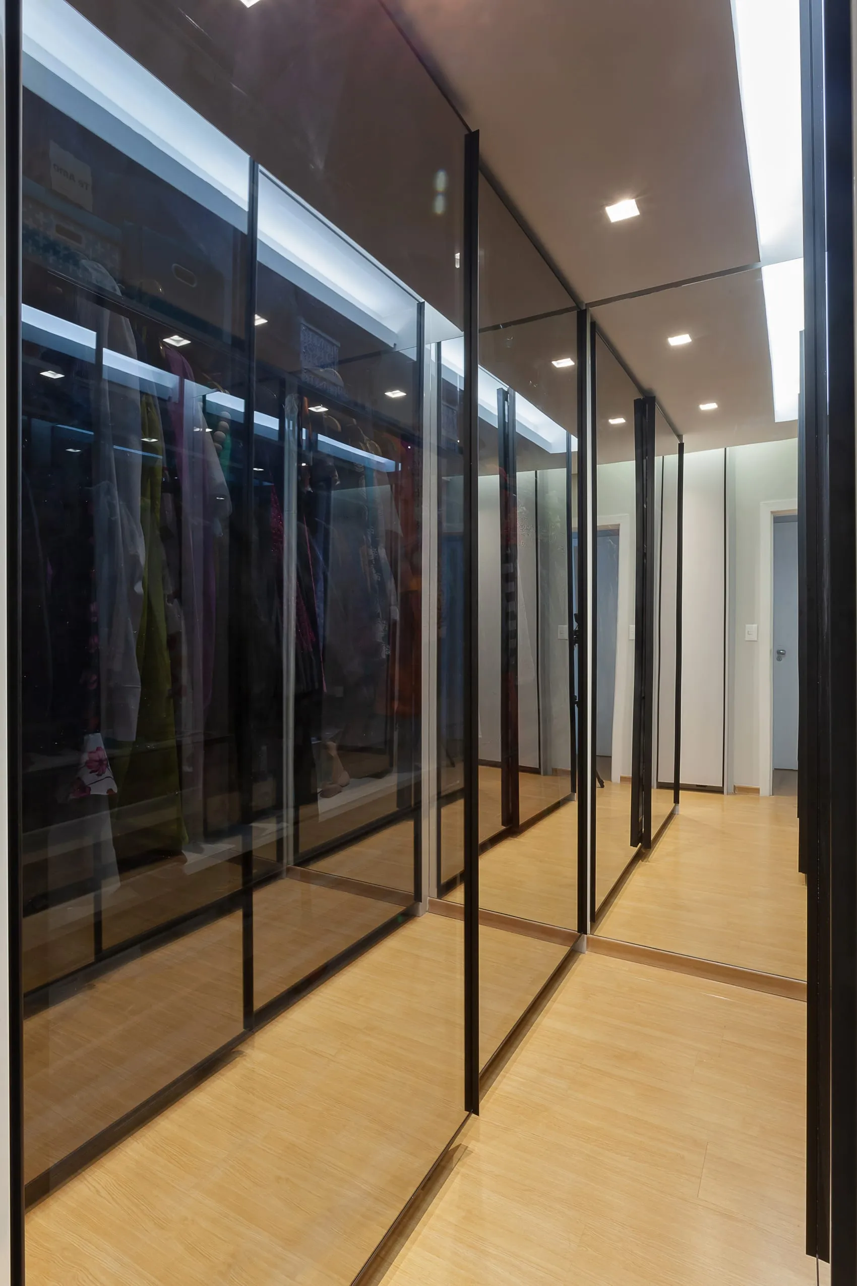 Closet com portas de vidro e perfil preto de alumínio, com roupas visíveis