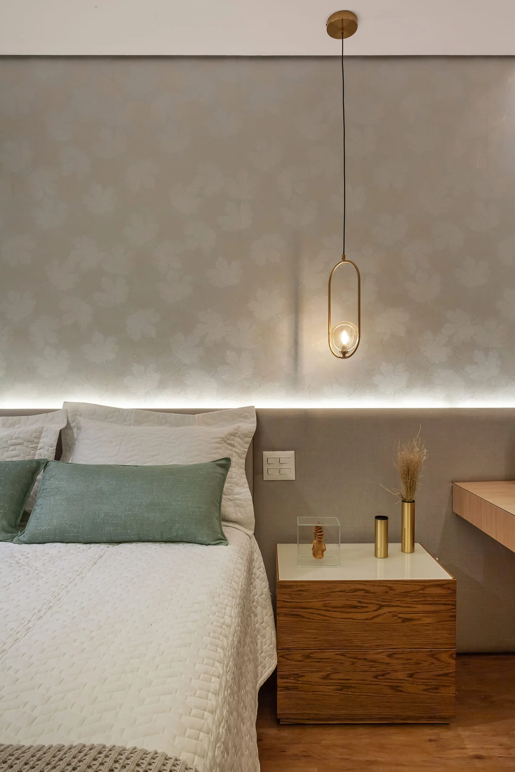 Detalhe da cabeceira do quarto com pendente dourado e almofadas verdes