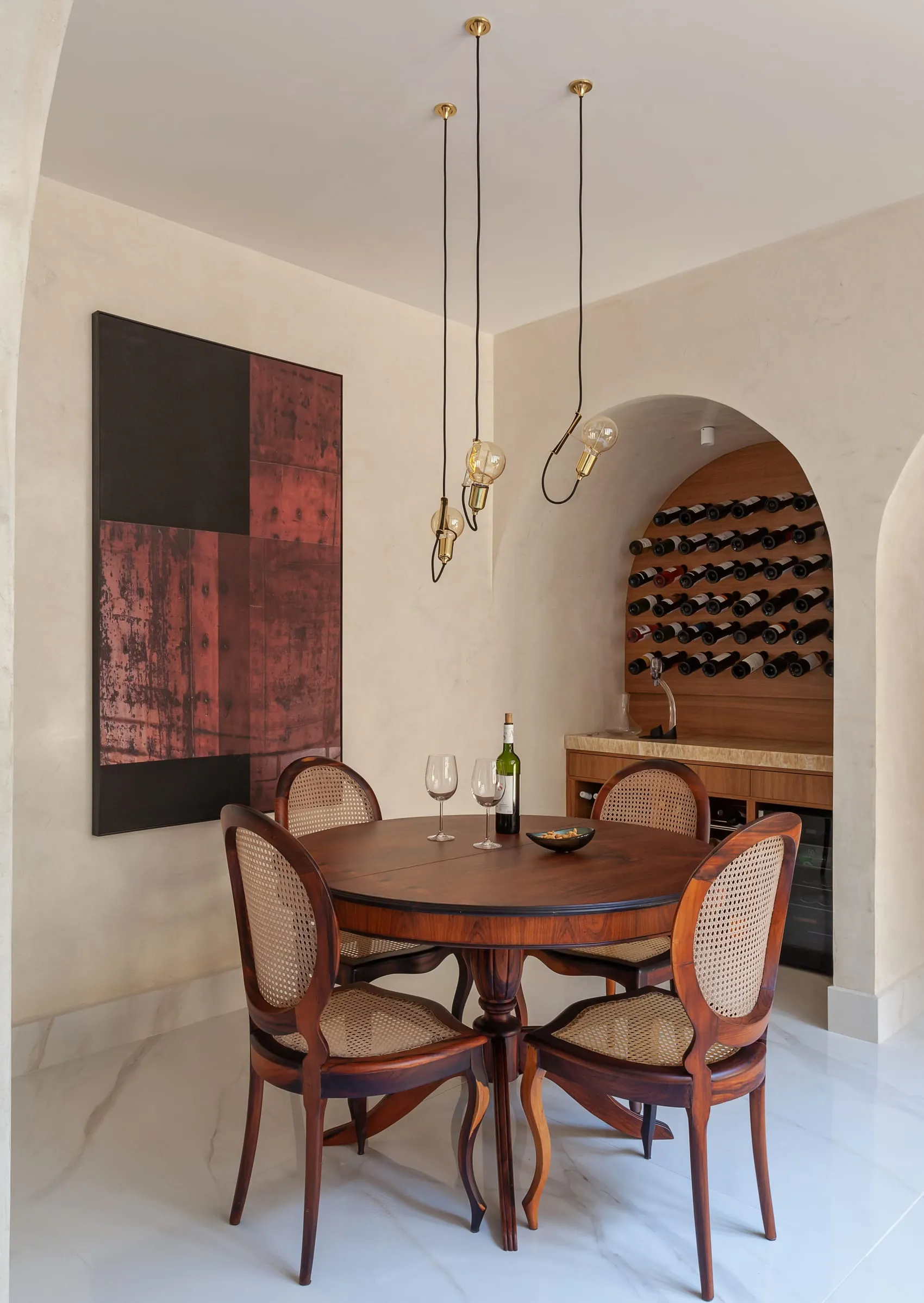Sala de jantar com mesa redonda de madeira, quadro abstrato e adega em arco ao fundo