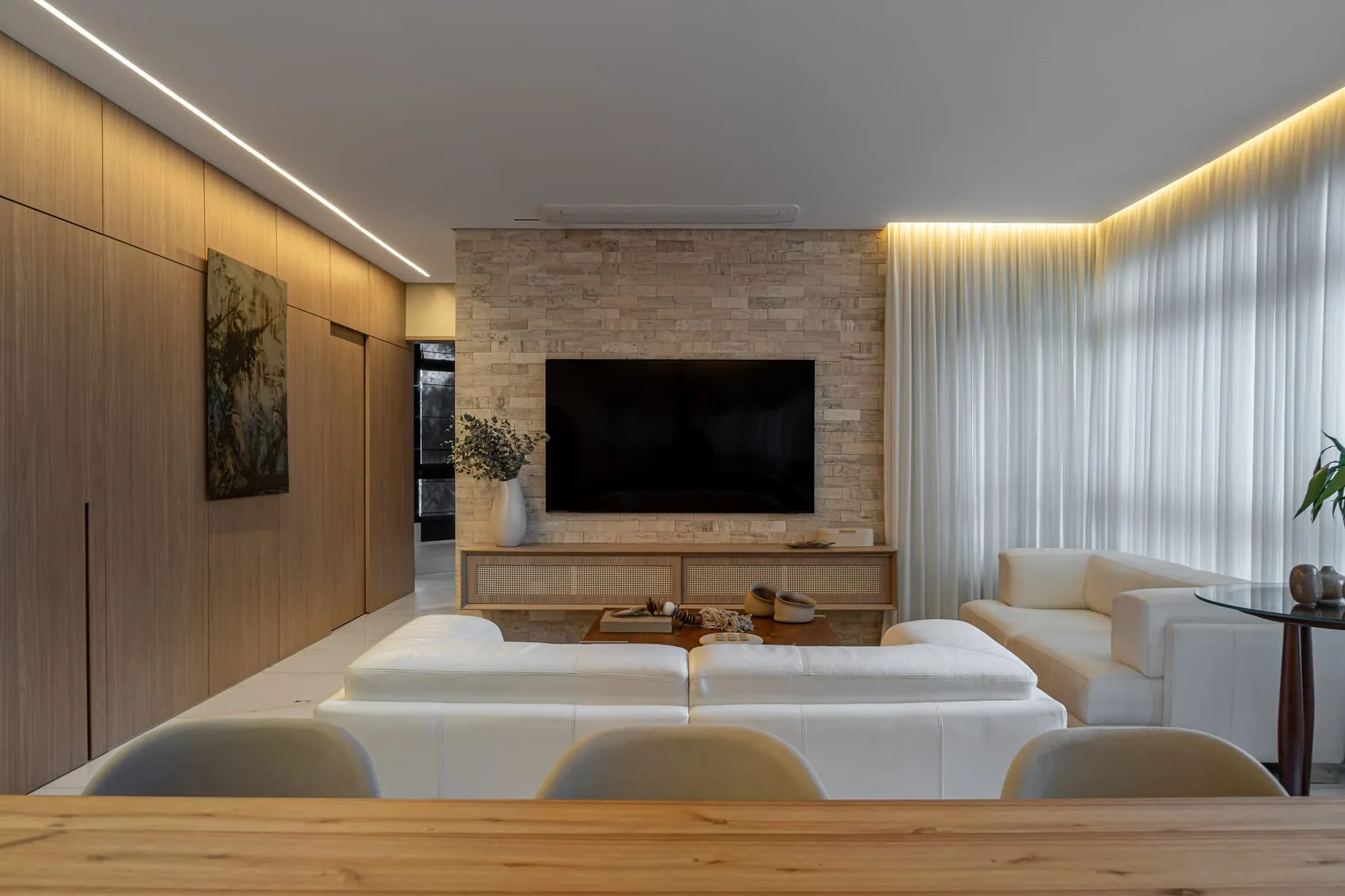 Sala de estar com painel de TV em pedra, sofá claro e marcenaria em madeira