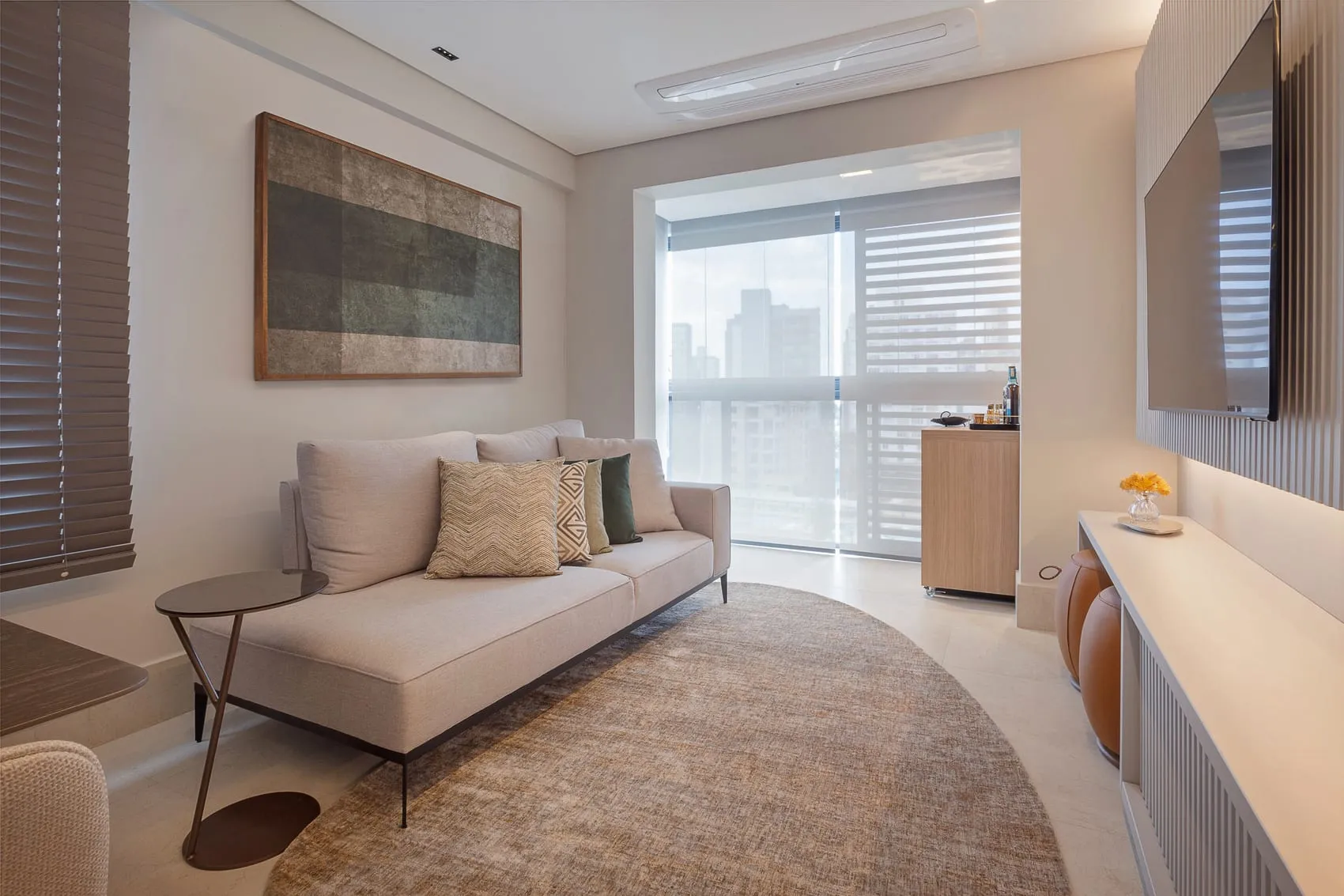 Sala de estar com sofá claro, tapete redondo, quadro e vista para a varanda