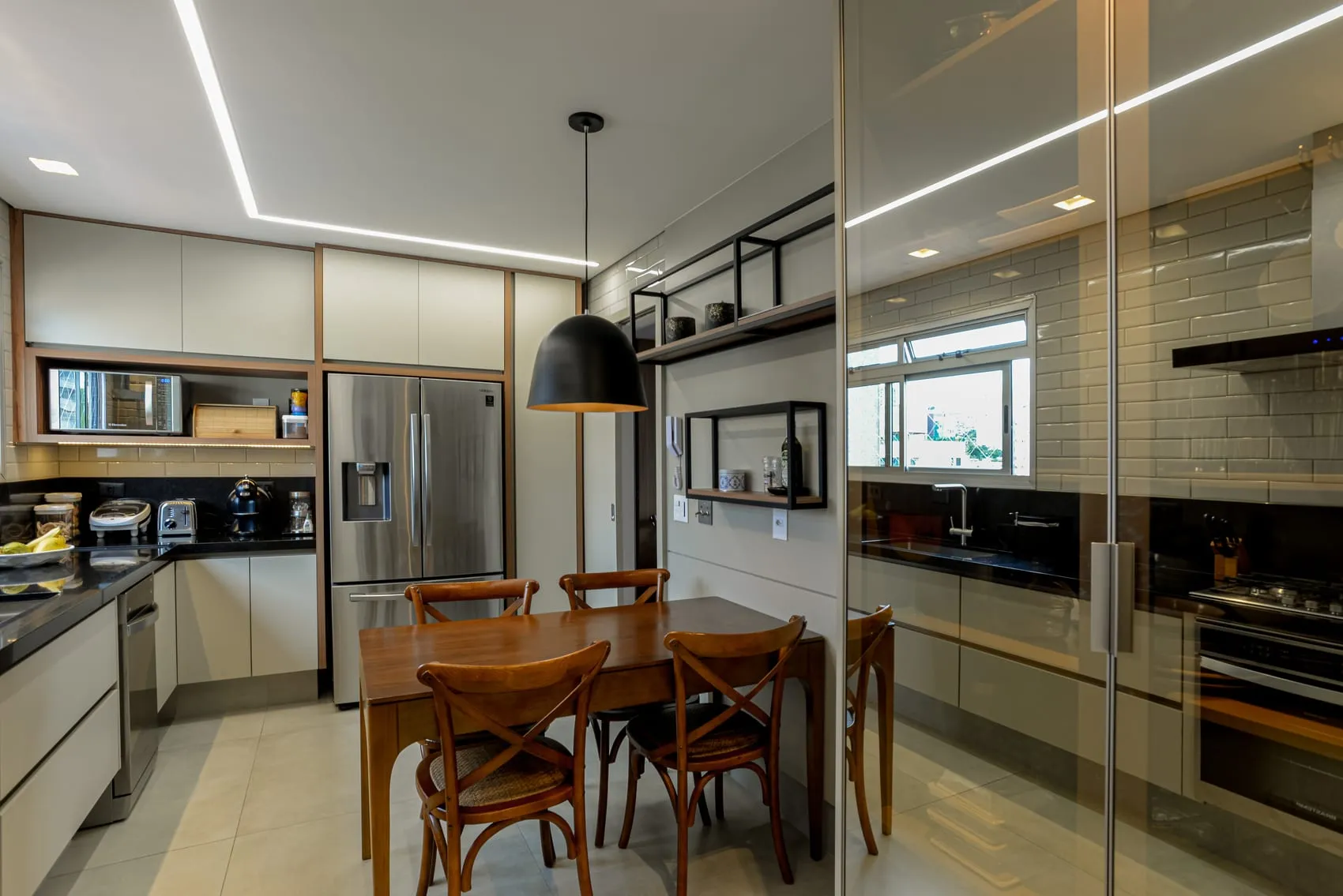 Cozinha com mesa de madeira, cadeiras, geladeira inox e pendente preto