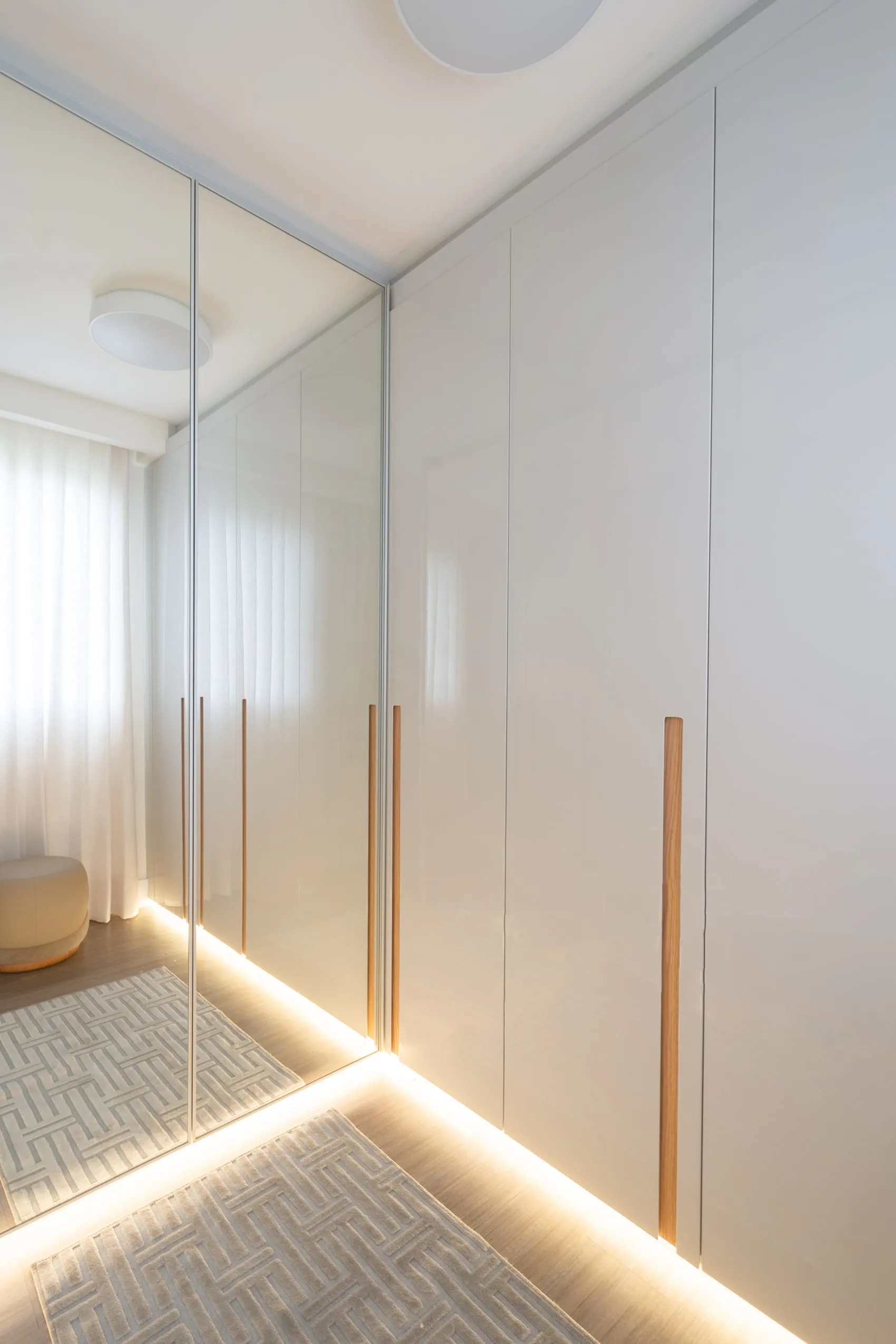 Closet com portas claras e puxadores verticais em madeira, com iluminação embutida