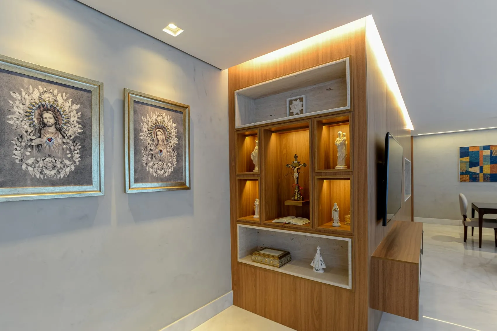 Hall com oratório iluminado embutido na marcenaria, entre dois quadros