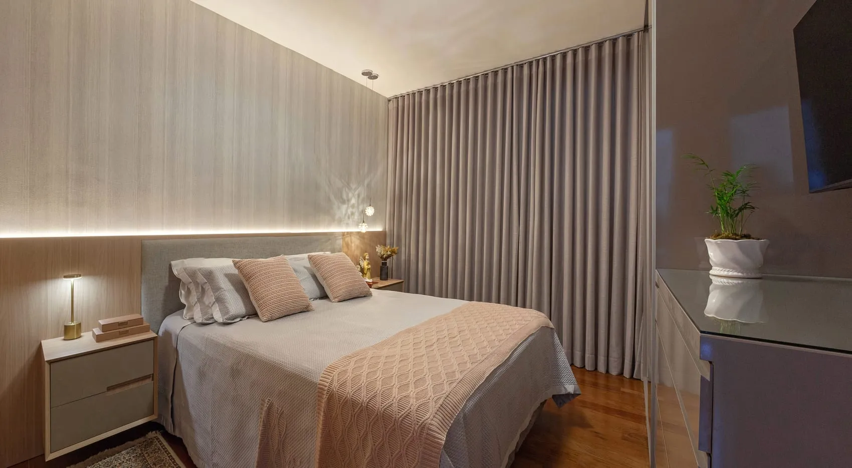 Quarto de casal com cortina, cabeceira em madeira clara e iluminação indireta no teto