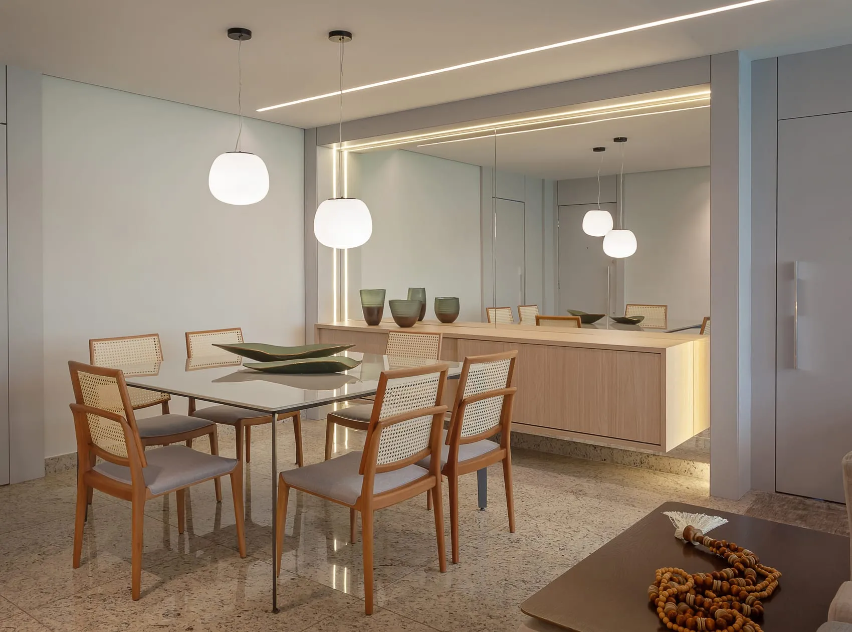 Sala de jantar com mesa quadrada, cadeiras de madeira e pendentes brancos