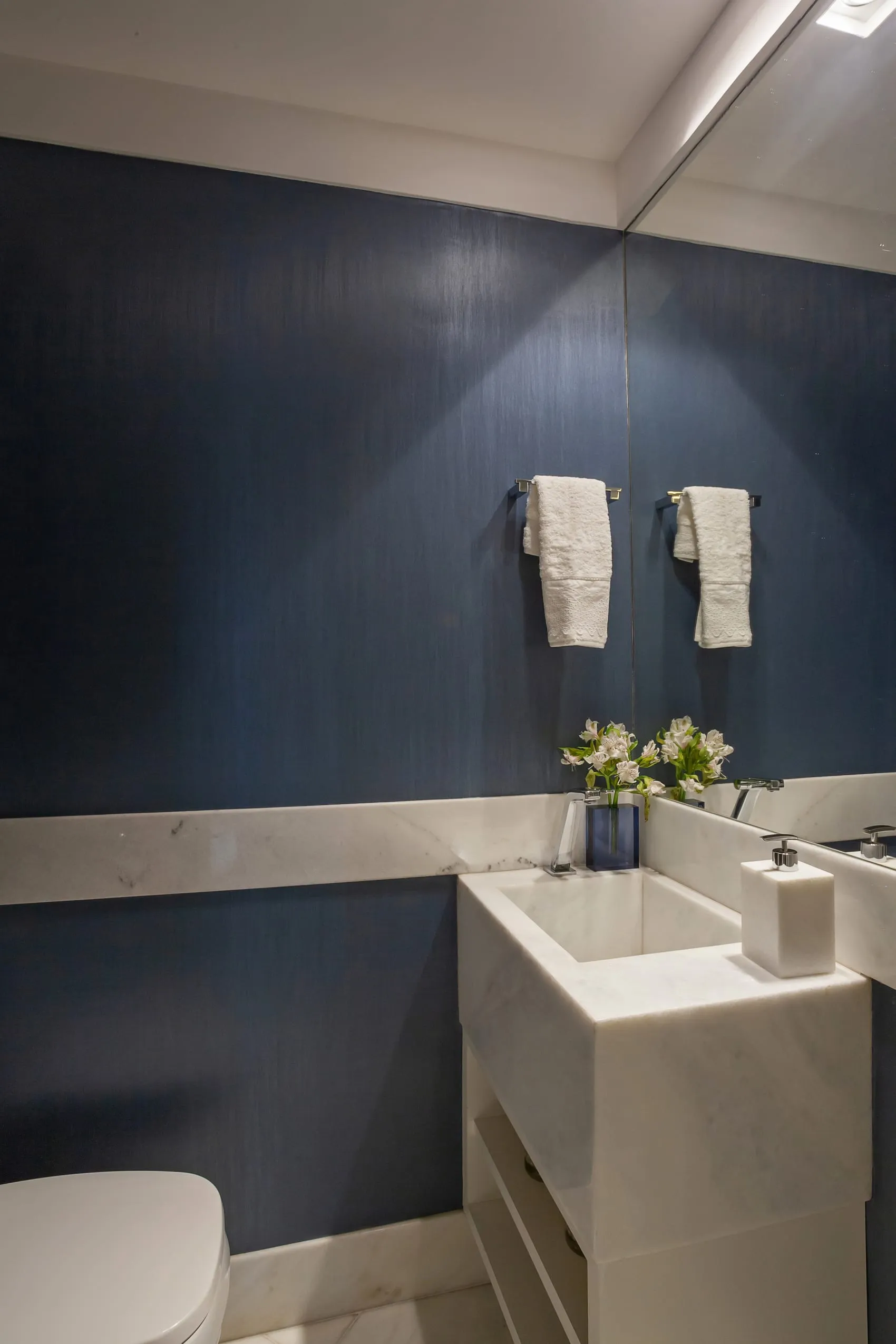 Banheiro com parede azul escura, bancada de mármore e toalheiros