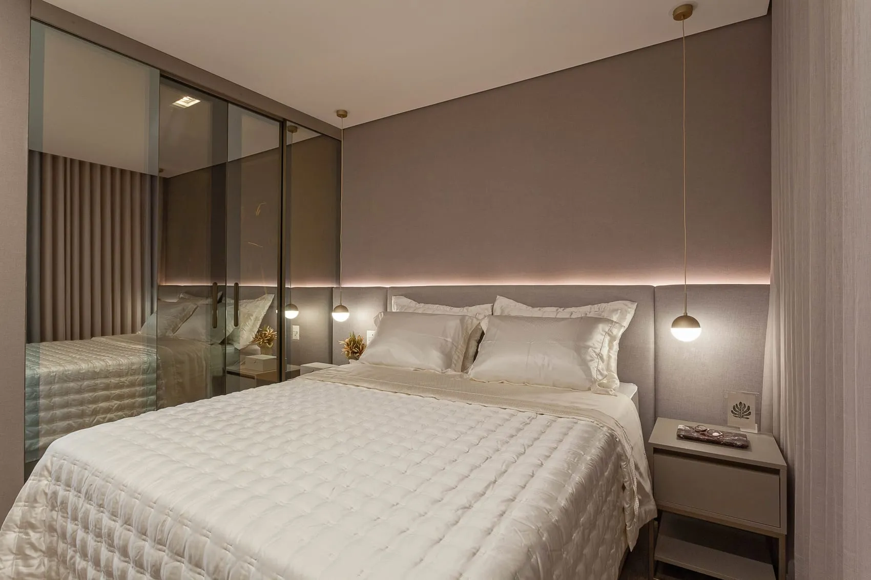 Suíte com cabeceira iluminada, roupa de cama branca e porta espelhada do closet