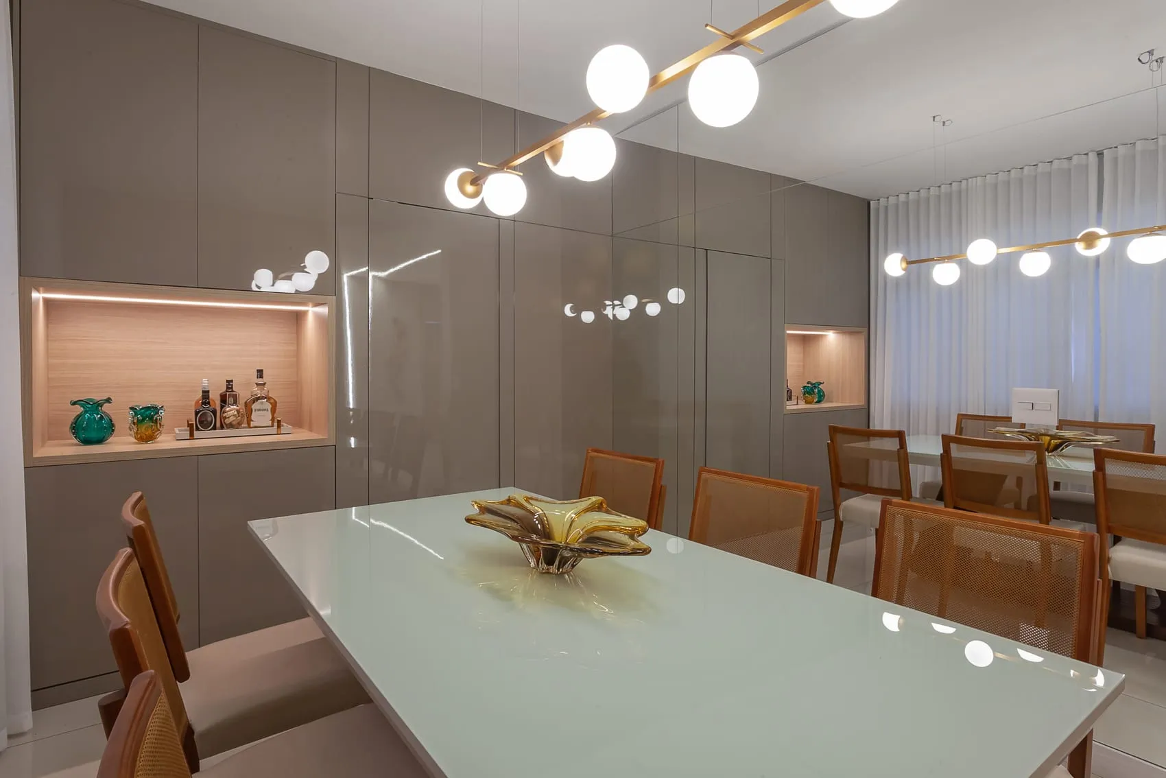 Sala de jantar com mesa de vidro, cadeiras de madeira e luminária de esferas