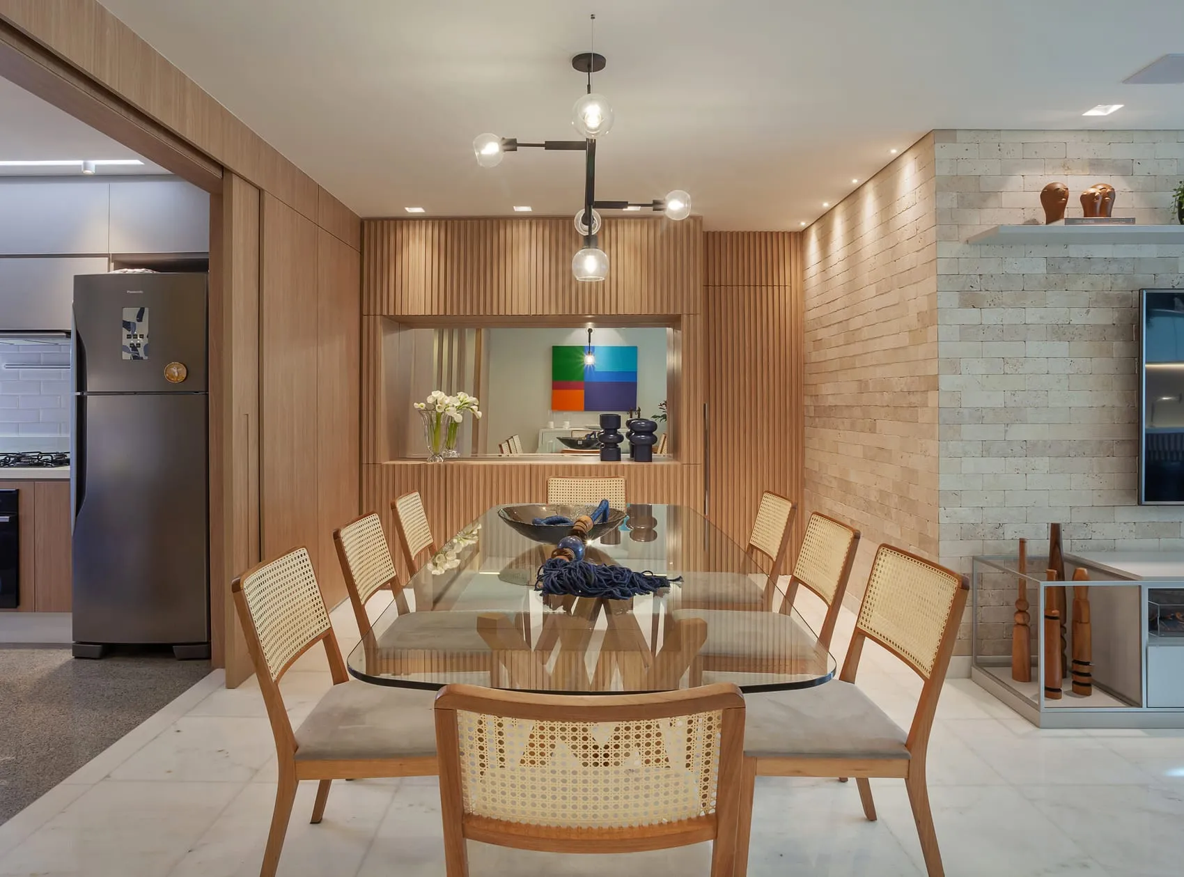Sala de jantar com mesa de vidro, cadeiras com palhinha e parede de pedra