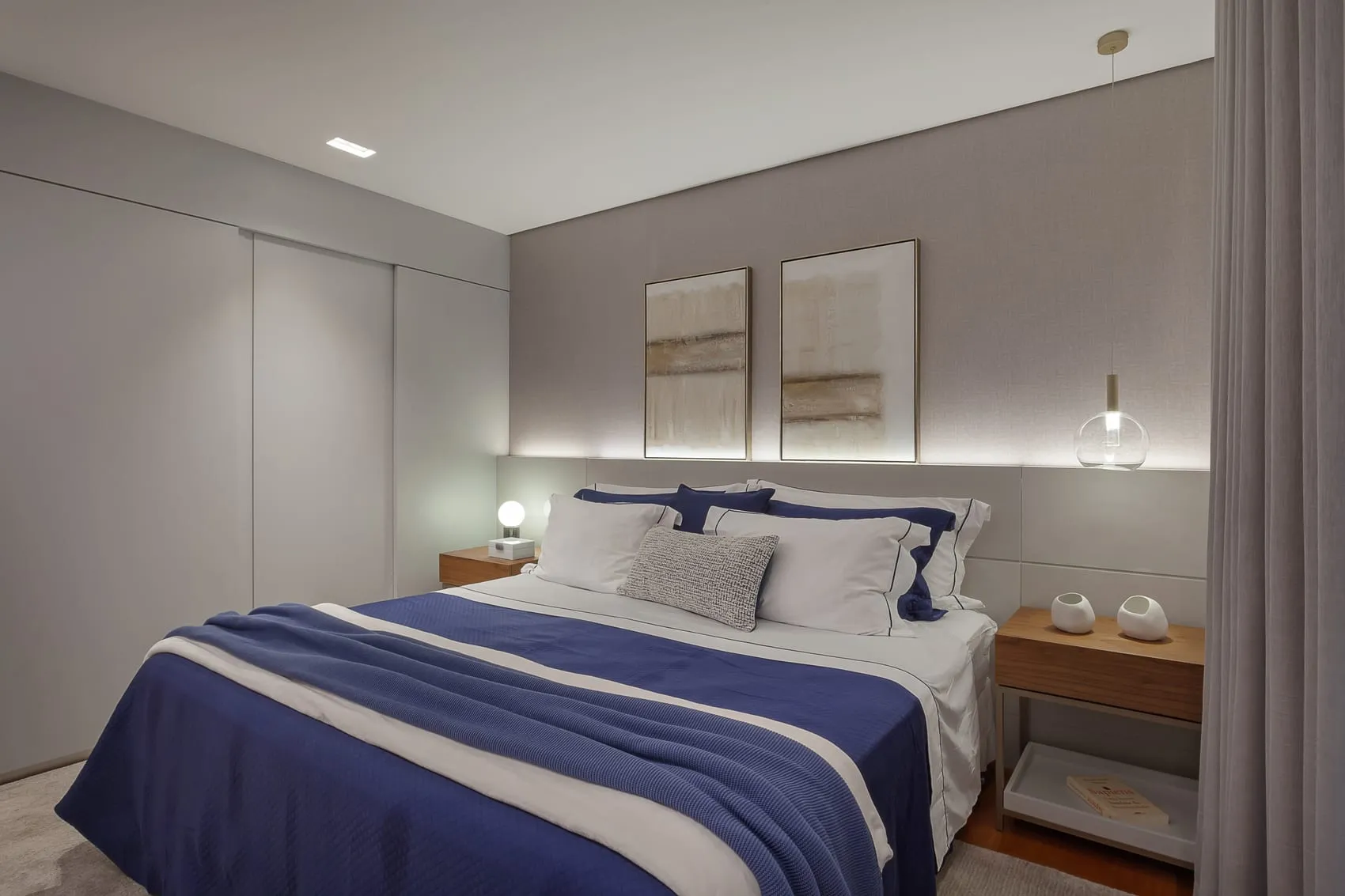 Suíte com cabeceira iluminada, roupa de cama azul e quadros na parede