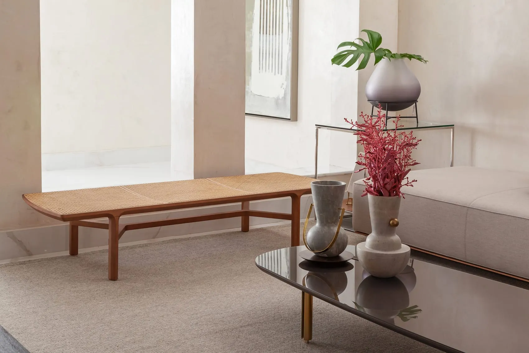 Detalhe da sala com banco de madeira, vasos escultóricos e mesa de centro espelhada