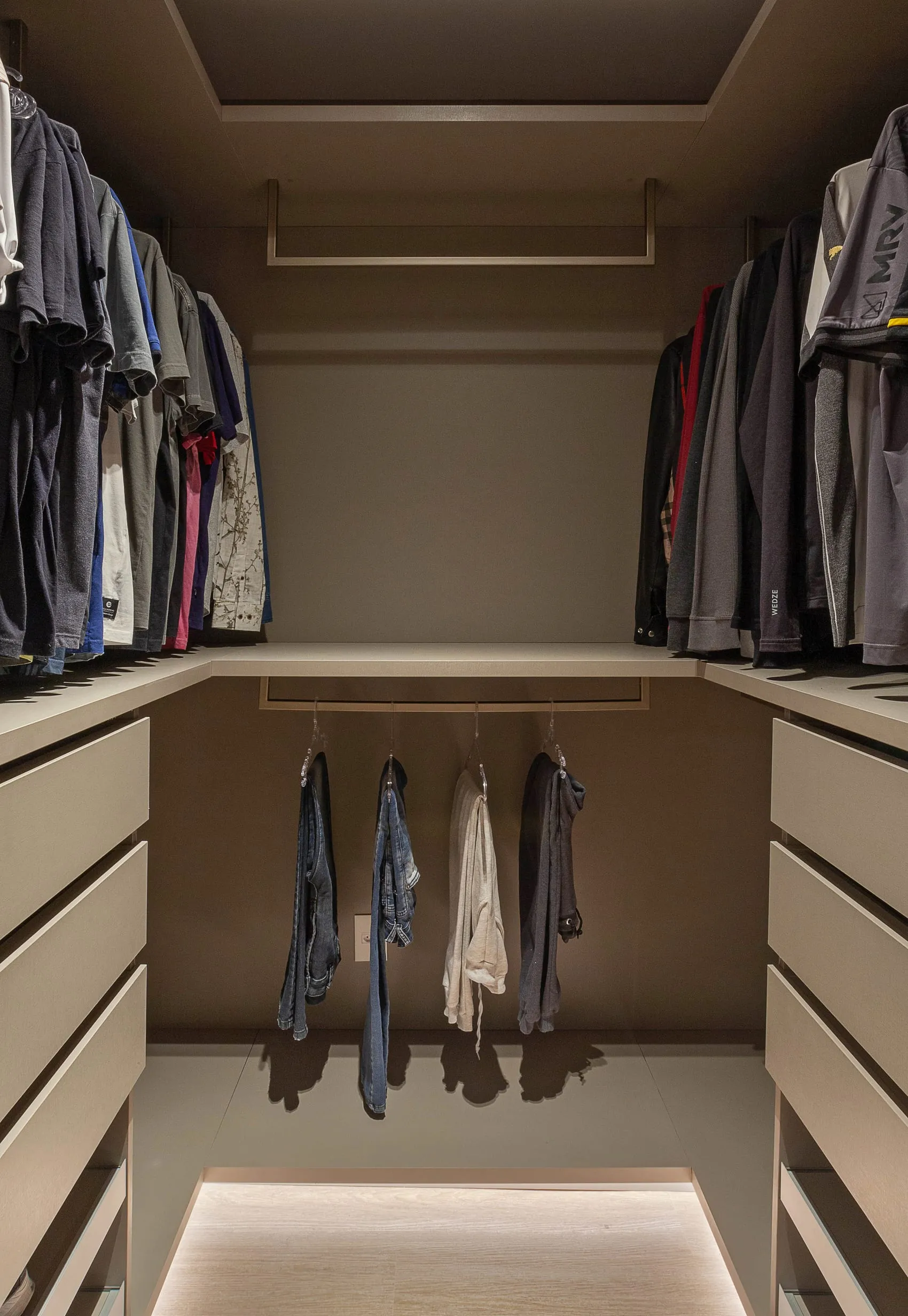 Closet aberto com araras de roupas, gavetas e iluminação interna