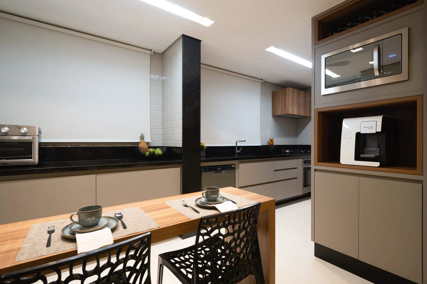 Cozinha com bancada preta, forno e micro-ondas embutidos e bancada de refeições