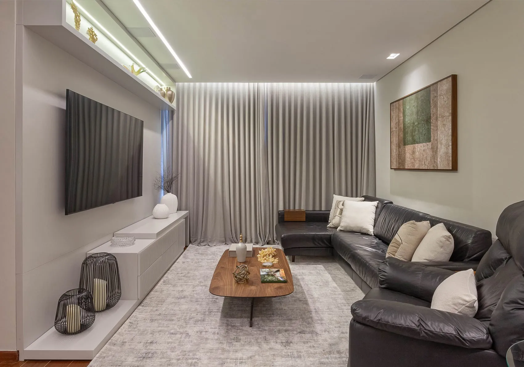 Sala de estar com sofá de couro escuro, painel de TV, cortina e tapete claro