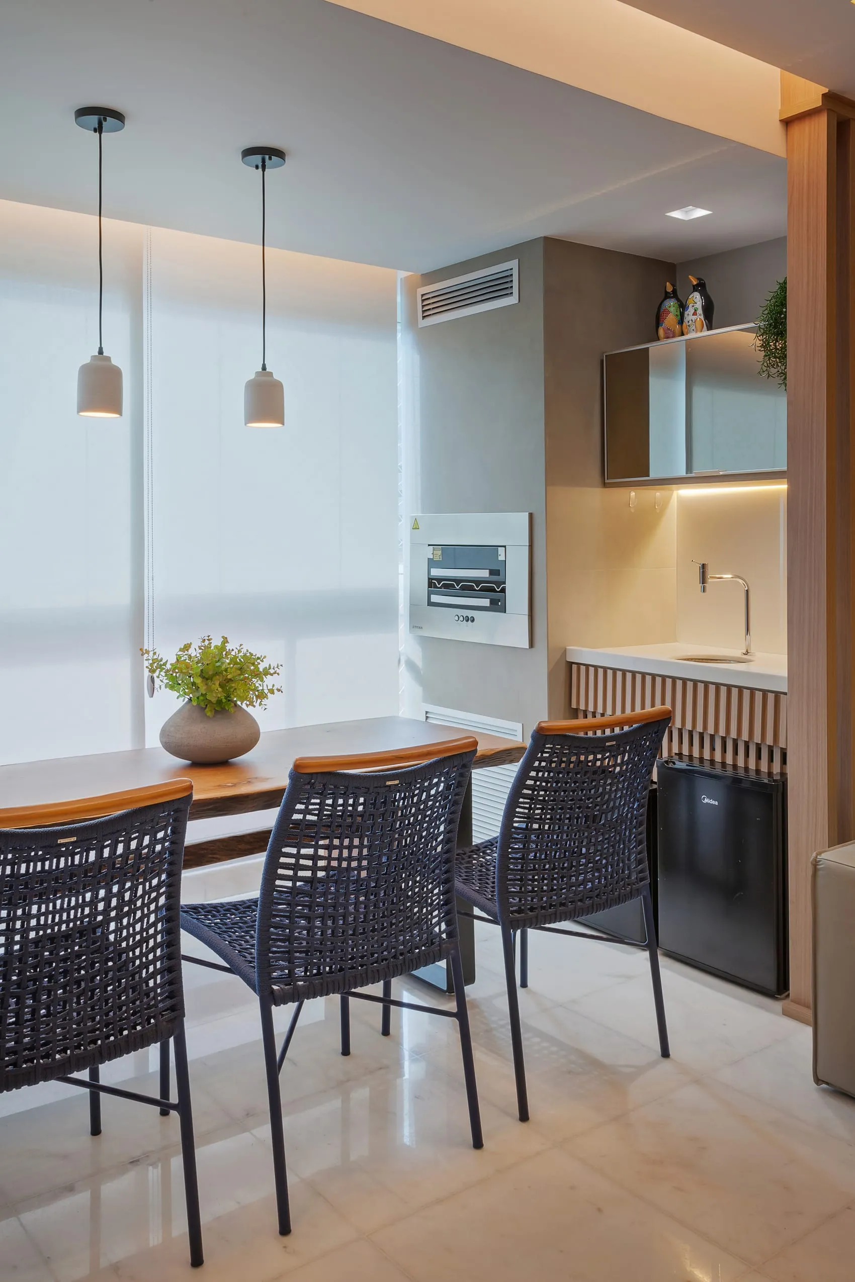Varanda gourmet com bancada, banquetas escuras e pendentes claros