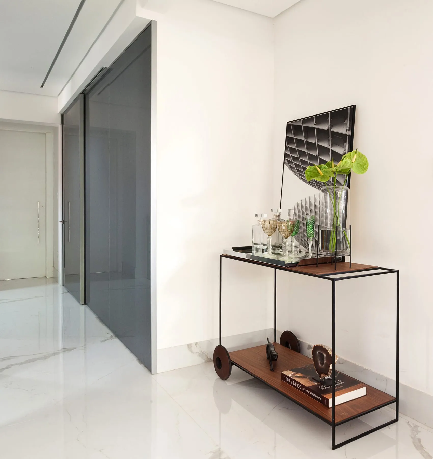 Hall de entrada com aparador metálico, vaso com folhagem e porta de vidro