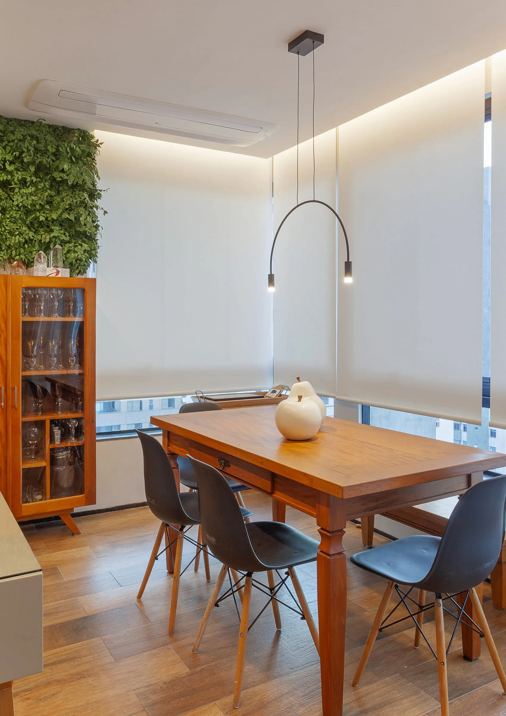Sala de jantar com mesa de madeira, cristaleira antiga e luminária de arco