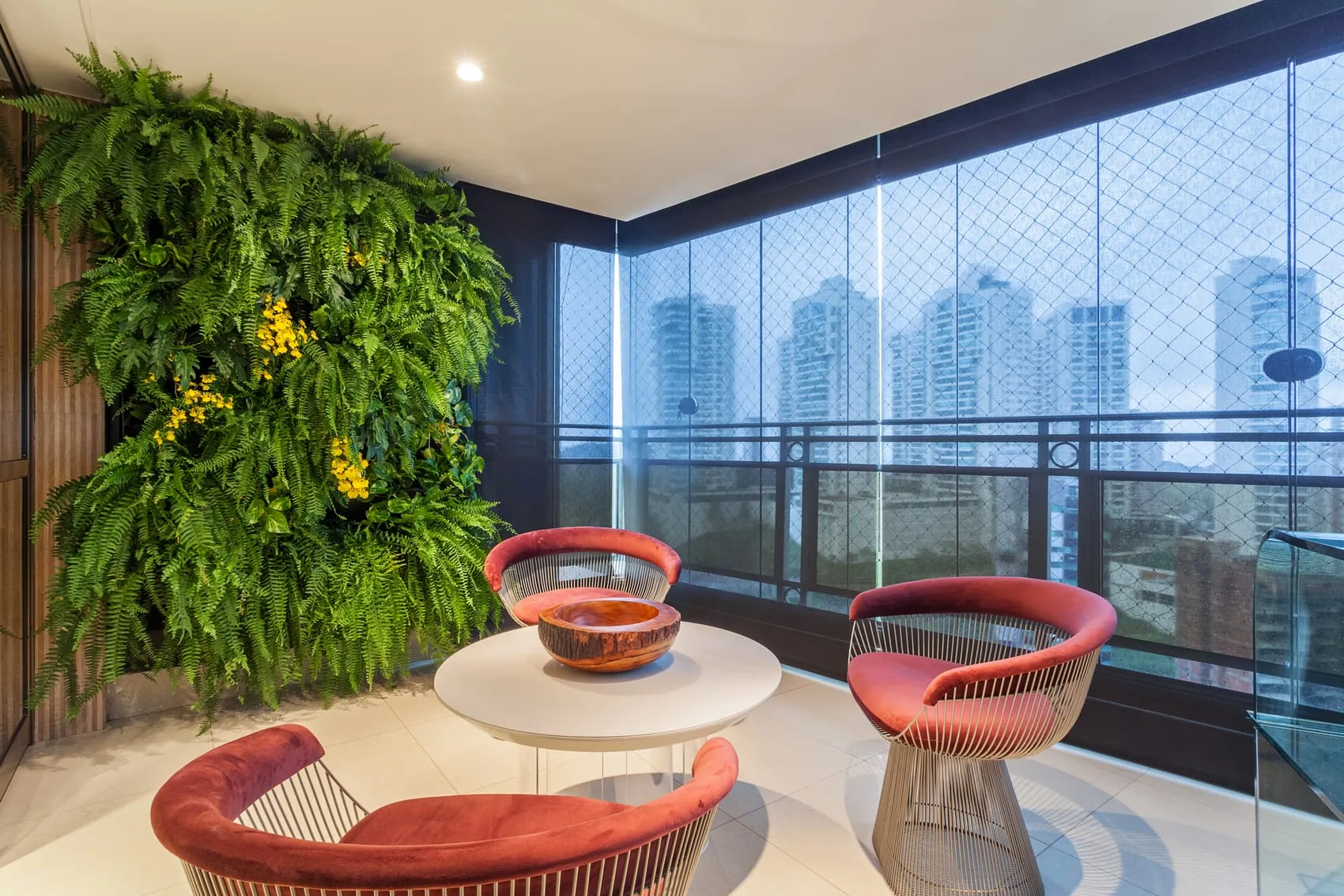 Varanda com jardim vertical, poltronas vermelhas e vista para os prédios