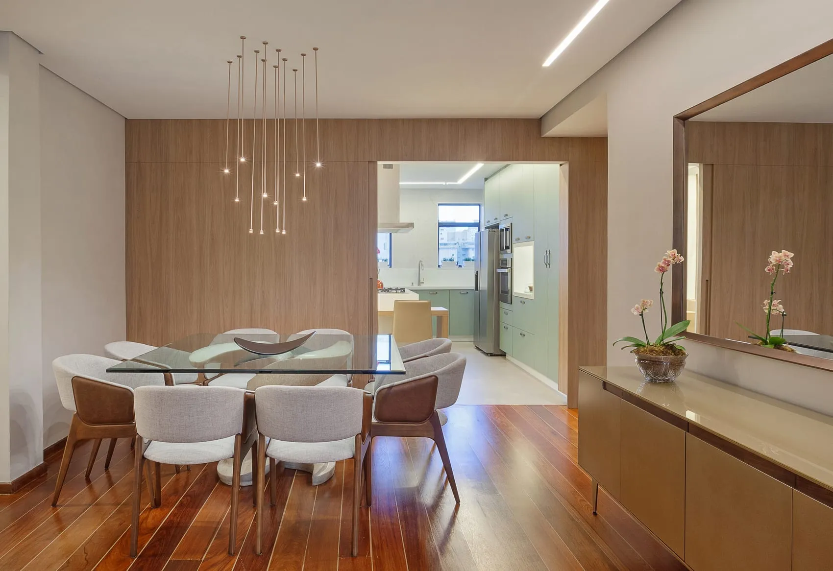 Sala de jantar com pendentes finos, painel de madeira, espelho e buffet