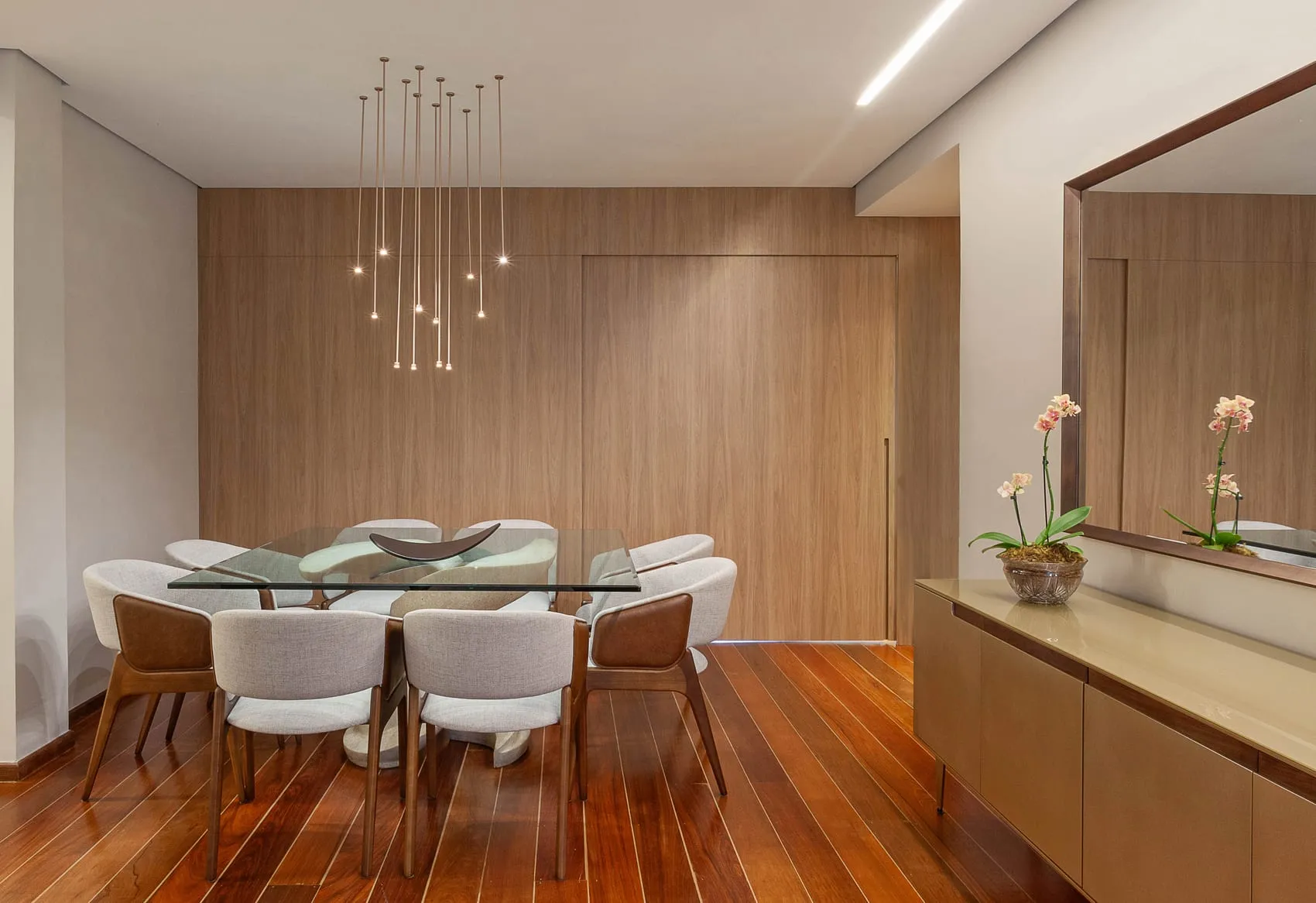 Sala de jantar em outro ângulo, com mesa de vidro e orquídeas sobre o buffet