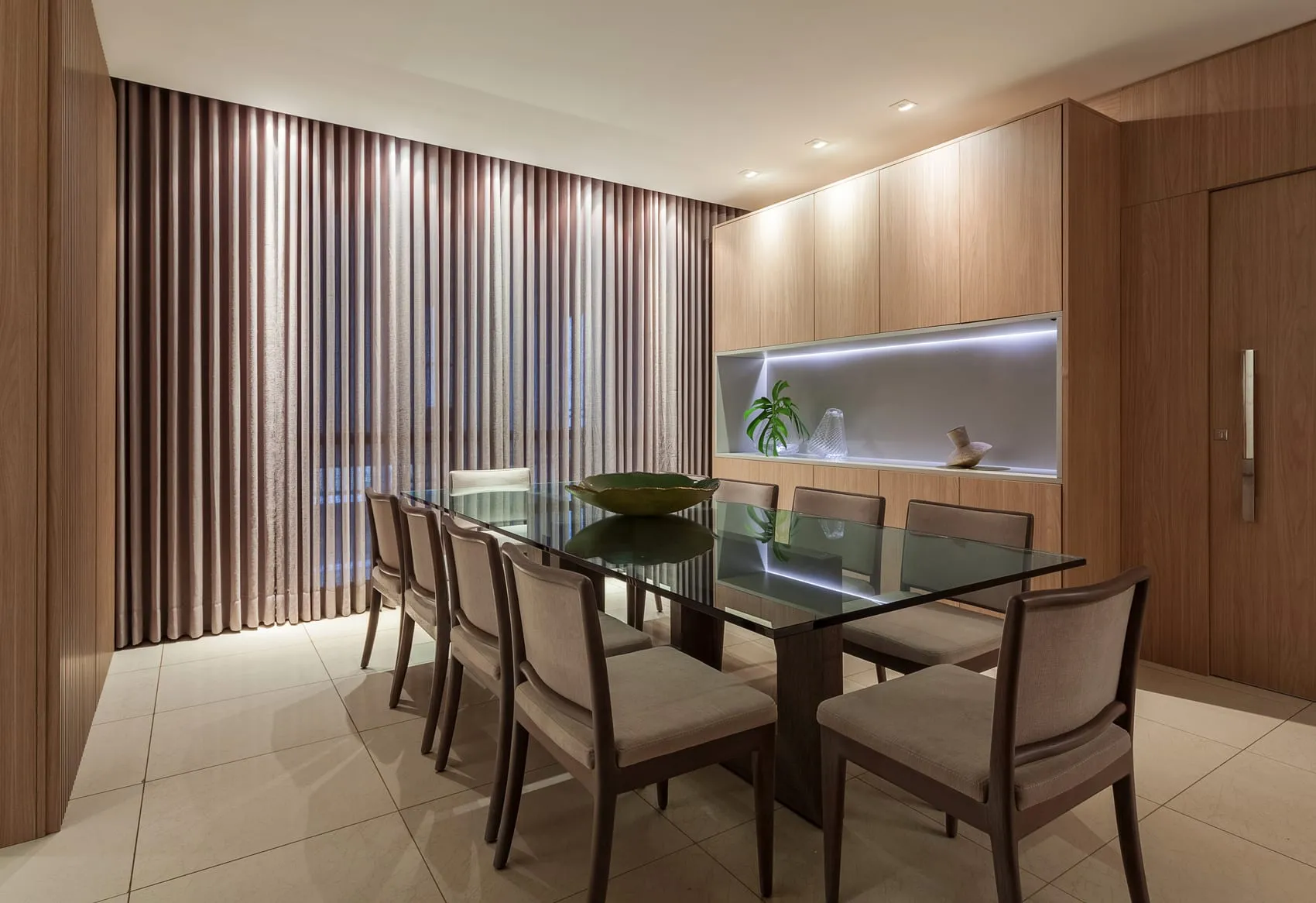 Sala de jantar com mesa de vidro, cadeiras estofadas e painel ripado em madeira