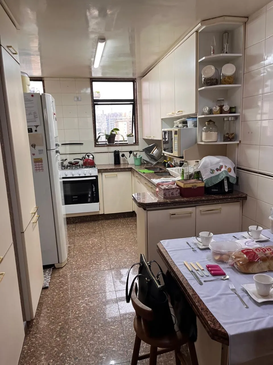 Cozinha antiga com armários brancos desencontrados e bancada cheia