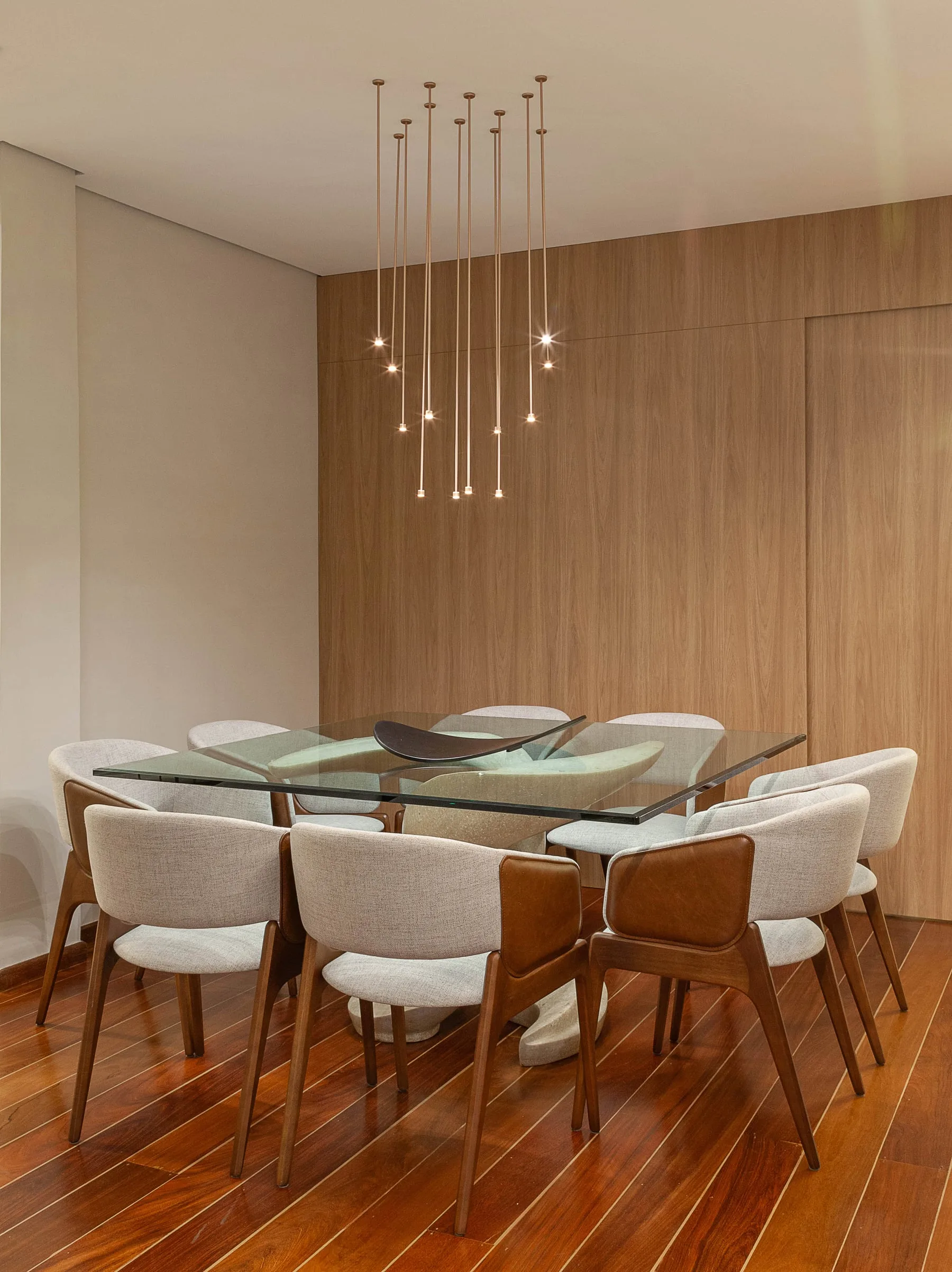 Sala de jantar com painel ripado em madeira, pendentes finos e cadeiras estofadas claras