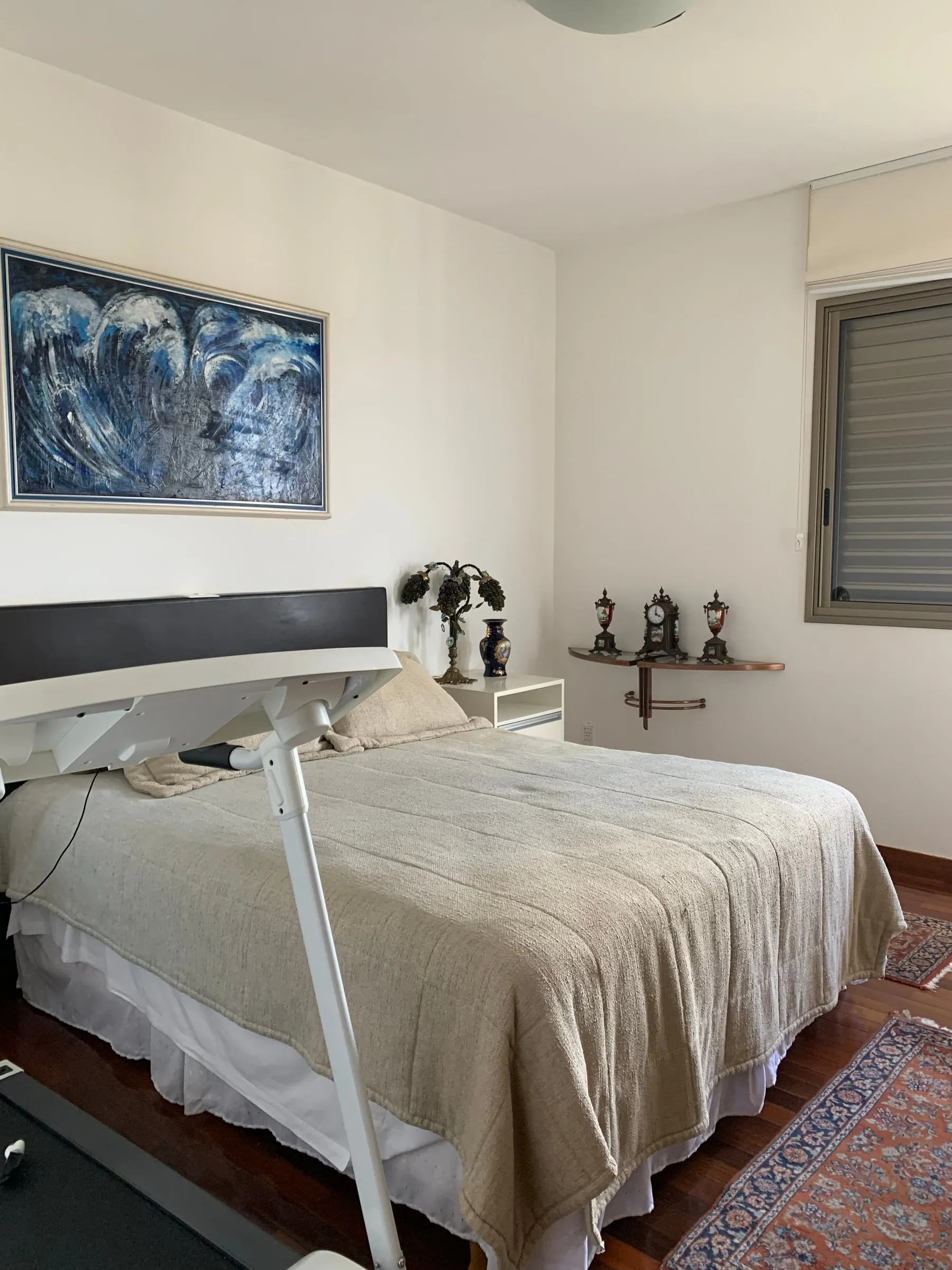 Quarto antigo com cabeceira escura, quadro grande e móveis avulsos