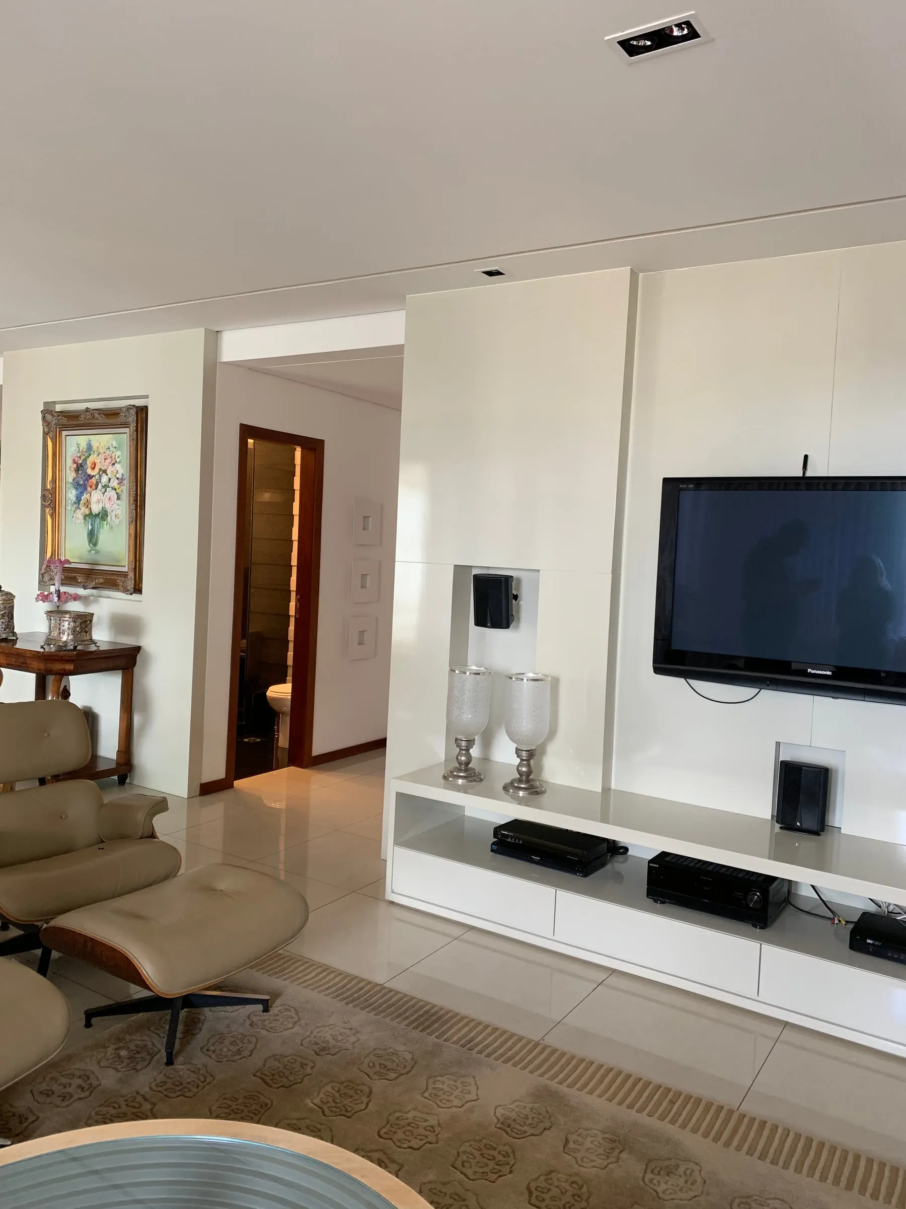 Sala antiga com painel branco, televisão e móveis pequenos encostados na parede