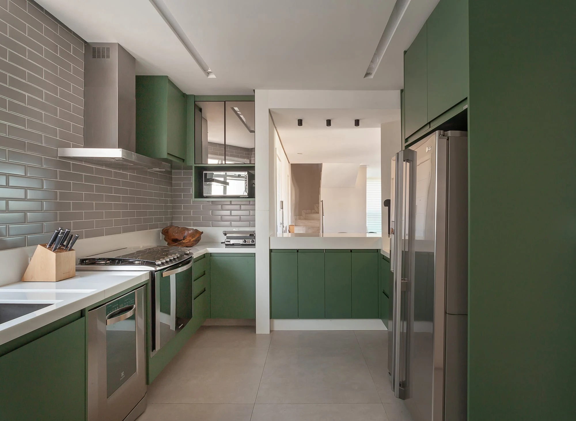 Cozinha com armários verdes, revestimento cinza e eletrodomésticos embutidos