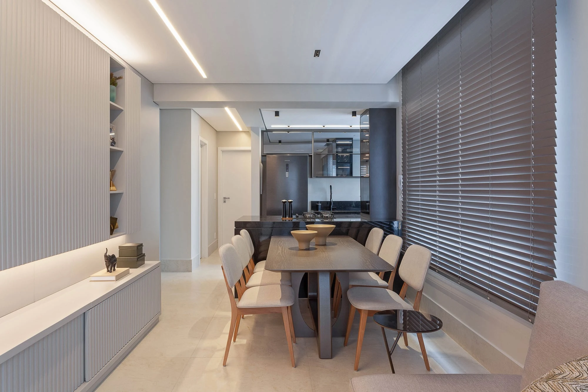 Sala de jantar com mesa alongada, cadeiras estofadas e persianas de madeira